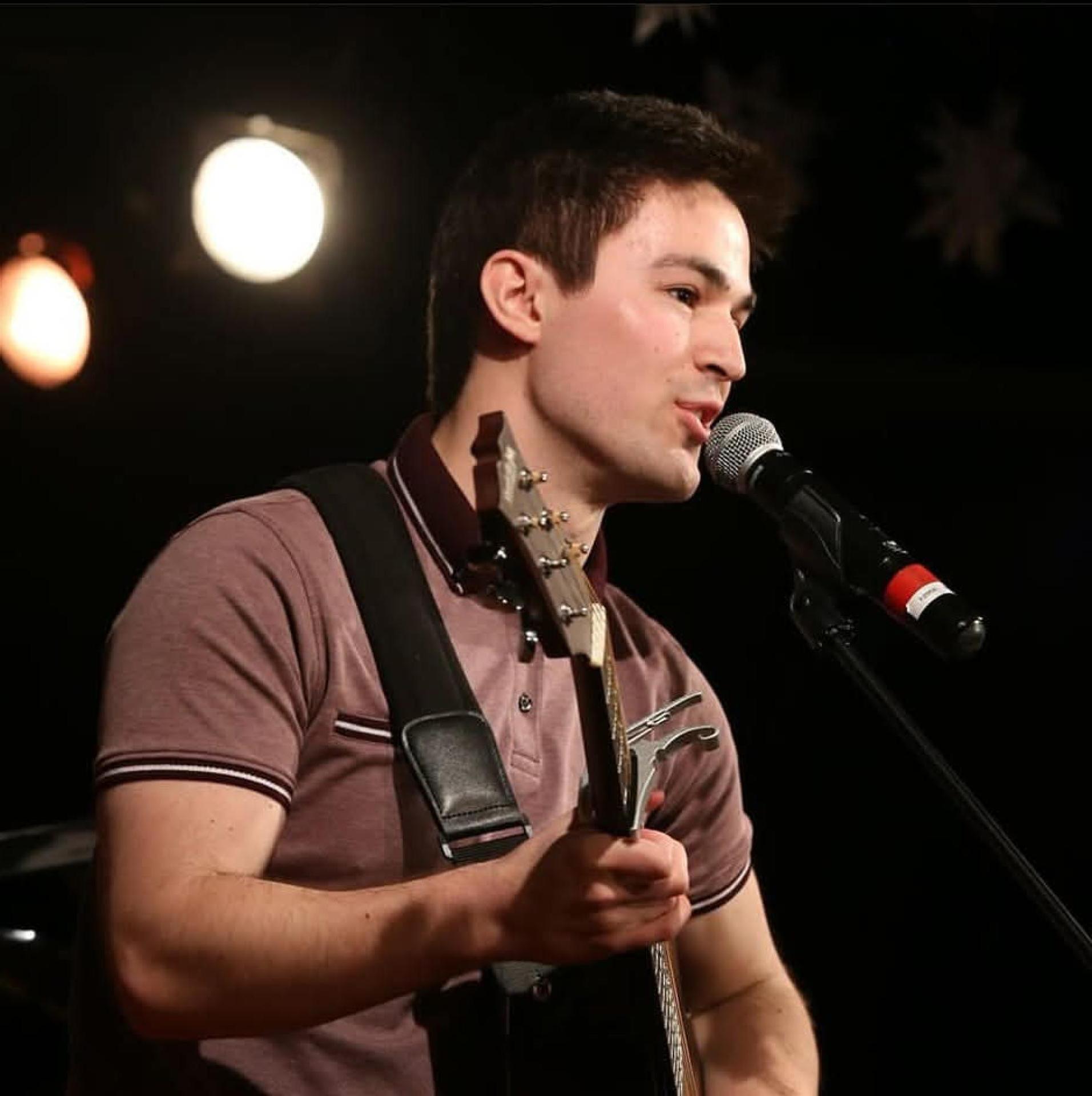 Ryan Heath singing into a microphone while holding a guitar
